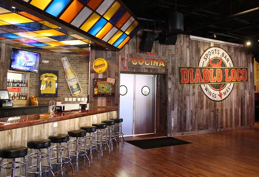 Bar area at Diablo Loco with reclaimed wood walls, a stained-glass canopy over the bar, and a Cocina entry to the kitchen