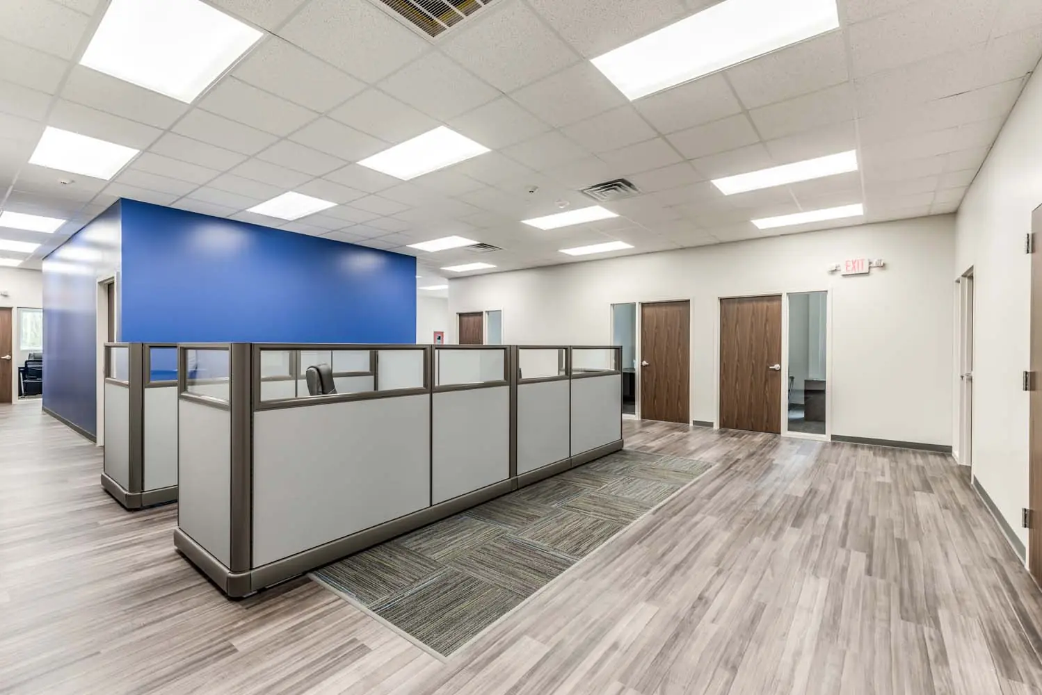 Wide view of the FSR Services open office with cubicles, blue accent wall, and private office doors along the perimeter