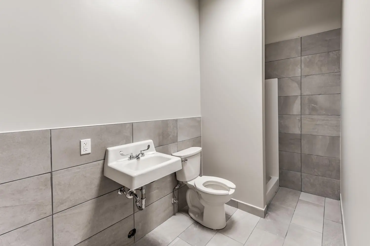 Restroom at FSR Services with gray tile wainscot, wall-hung sink, and walk-in shower stall