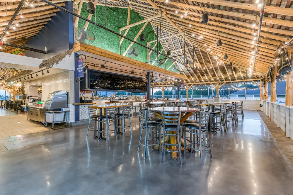 Interior of LaBrisa showing the central bar under a thatched palapa roof with exposed timber framing, polished concrete floors, and high-top dining