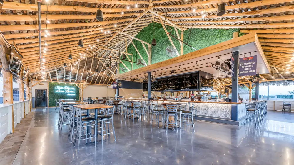 Wide view of LaBrisa interior with bar, communal dining, boxwood feature wall, and exposed wood roof structure