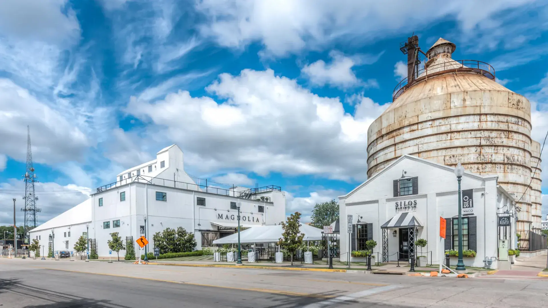 Magnolia Market at the Silos street view in Waco, TX with the white Magnolia warehouse, event tent, and iconic Brazos Valley Cotton Oil Company silo