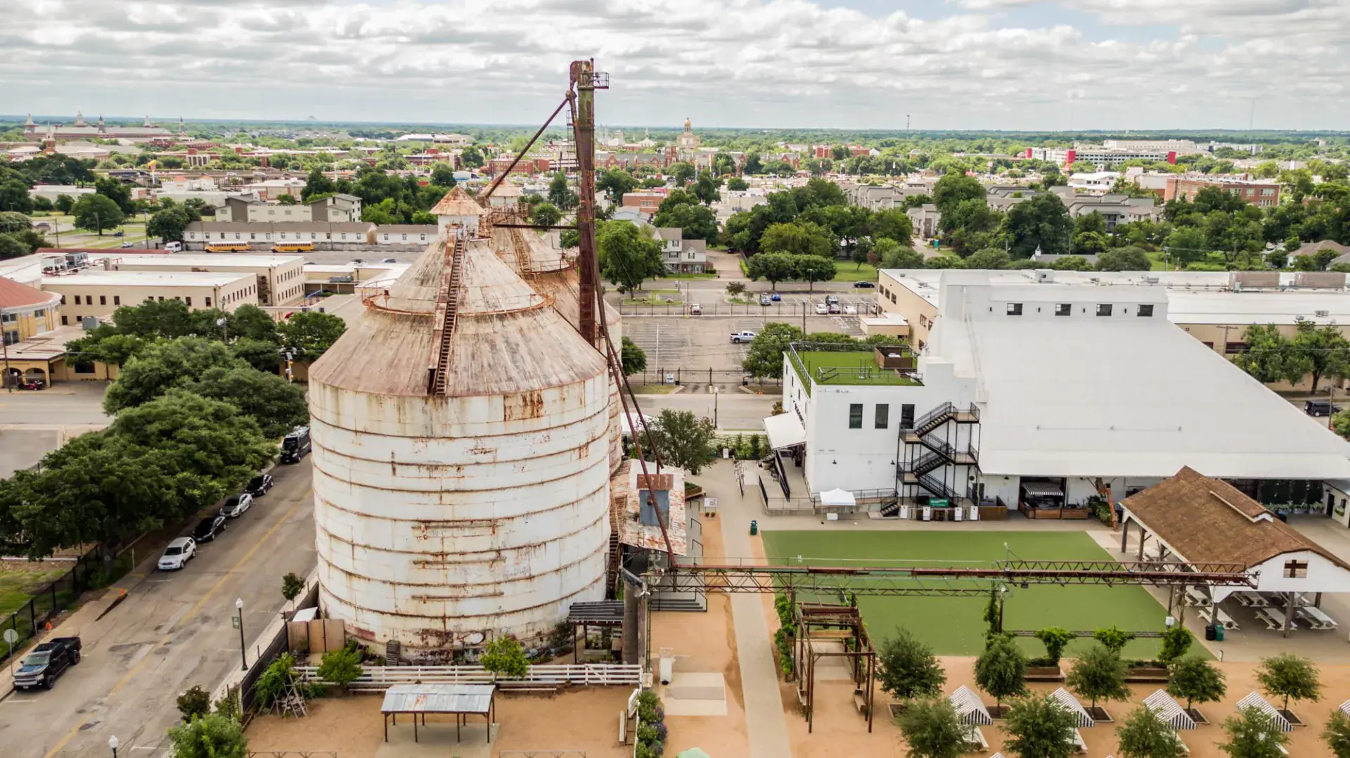 Aerial view of the Magnolia Market courtyard with twin silos, turf lawn, food truck area, and rooftop terrace on the main warehouse