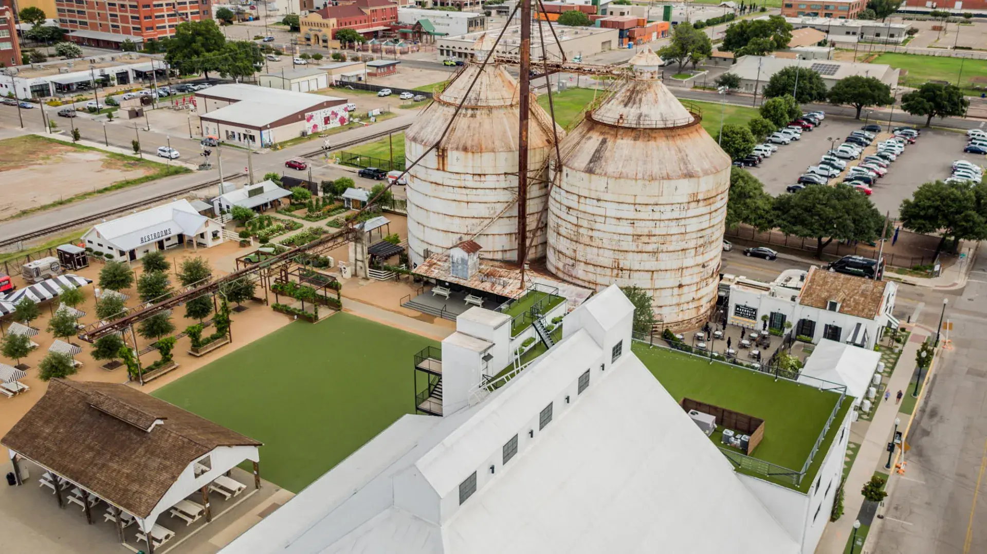 Overhead aerial of the Magnolia Market silos, event lawn, rooftop turf terraces, and adjacent Silos Baking Co. building in downtown Waco
