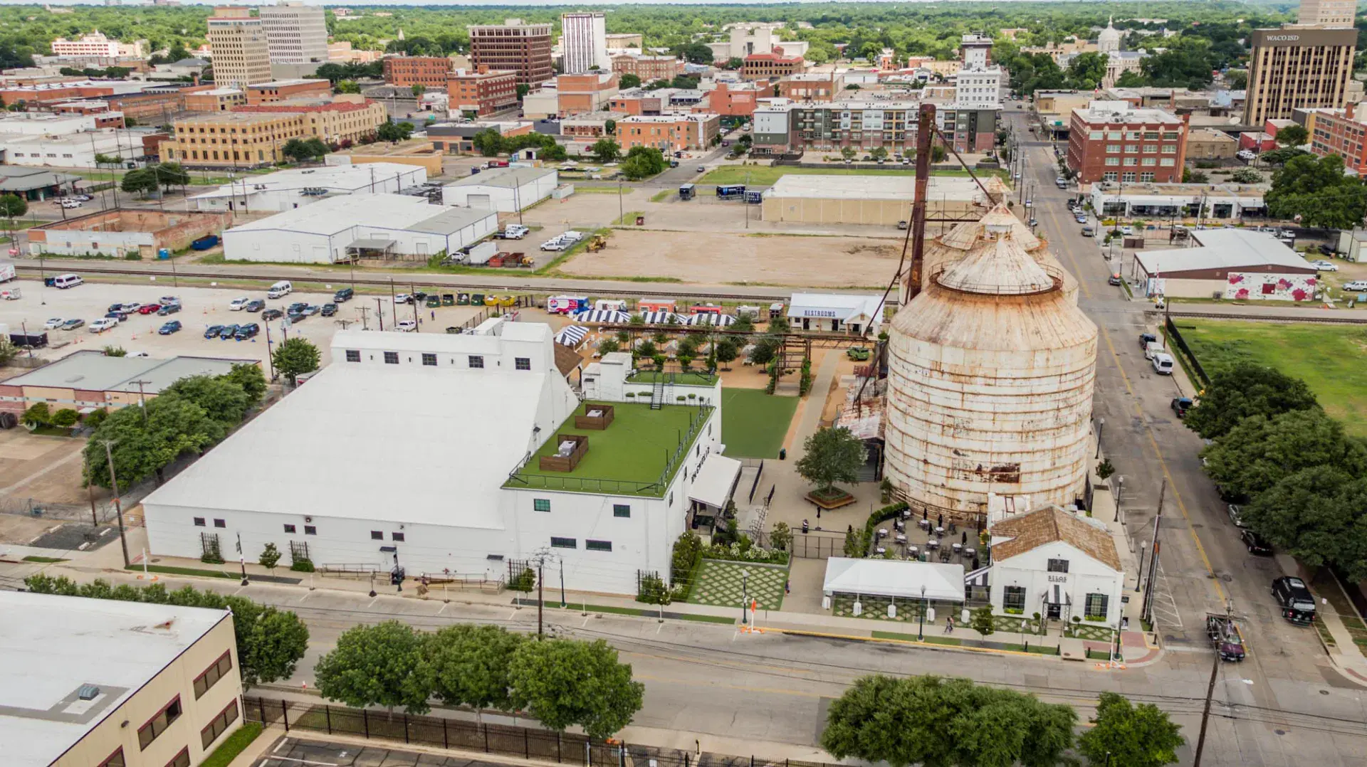 Long aerial view down the Magnolia Market block in downtown Waco, TX with the silos, Silos Baking Co. brick building, event tent, and patterned hardscape entry