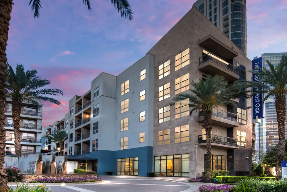 Post Oak Apartments mid-rise facade in Houston at dusk with palm trees and porte cochère entry