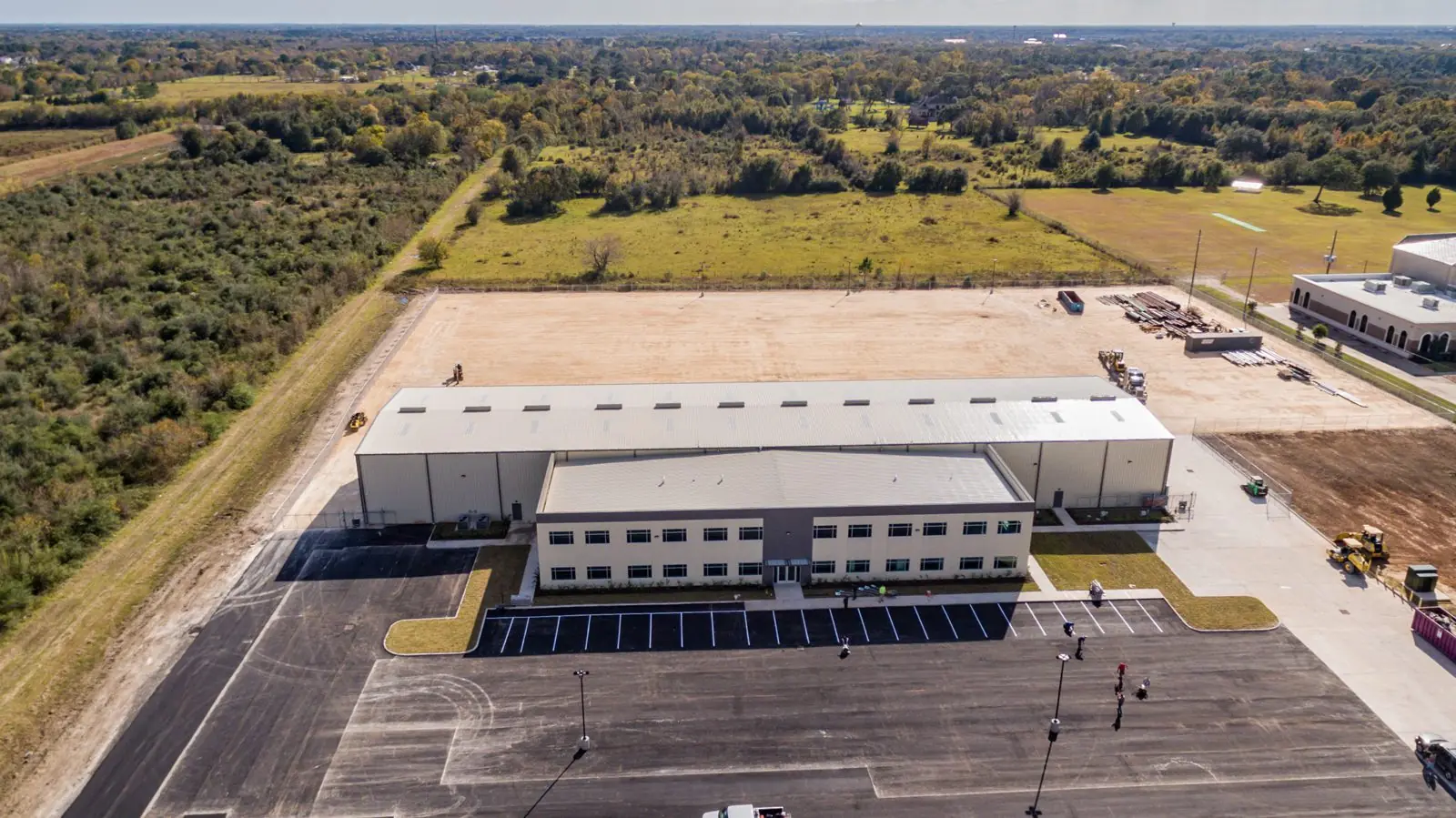Long aerial view of the Repcon Industrial complex with the two-story office, attached warehouse, lay-down yard, and adjacent industrial neighbors