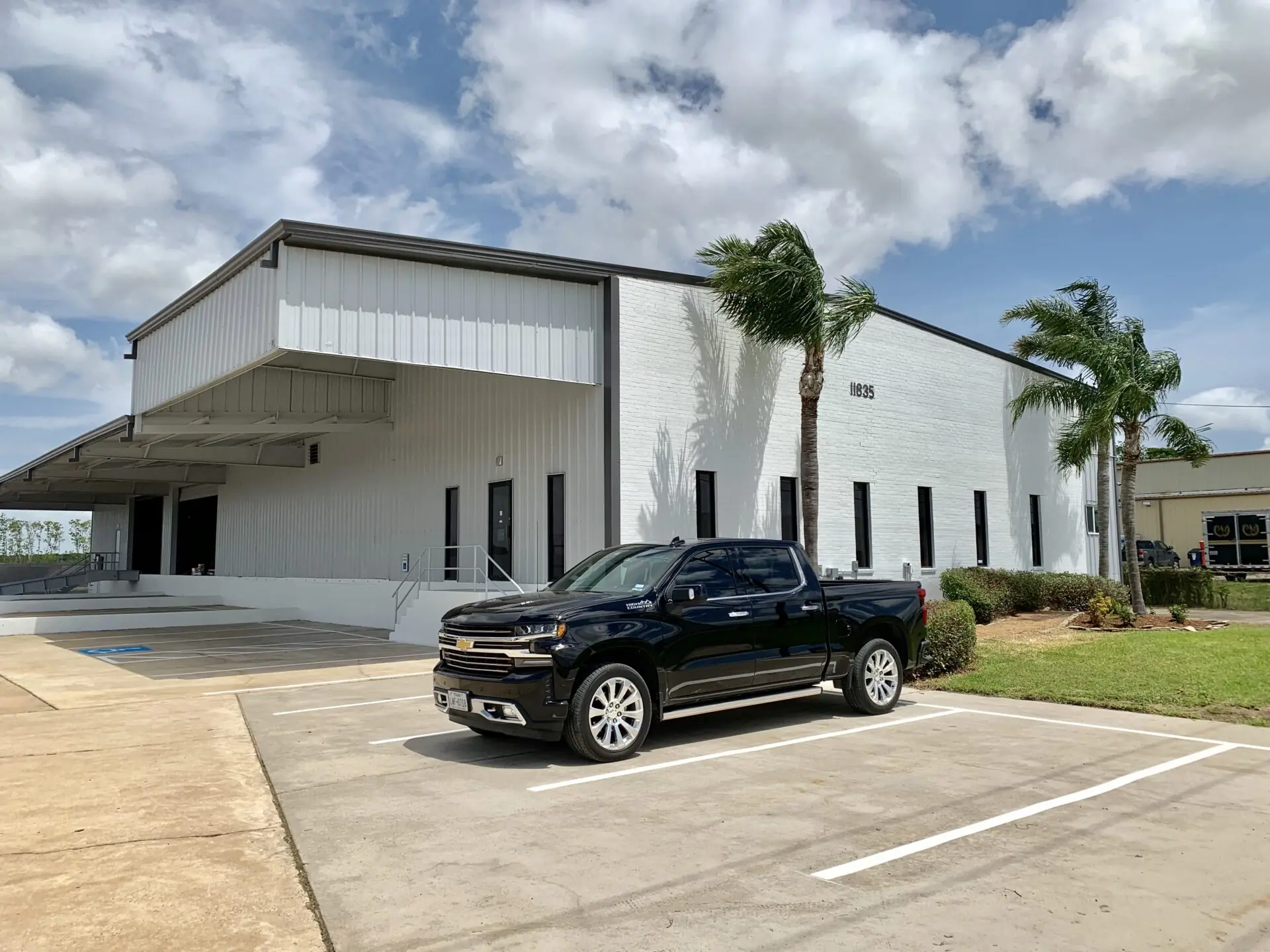 Exterior of Summit Industrial's renovated facility in La Porte, TX with white brick veneer, metal siding, covered loading area, and palm trees flanking the main entry