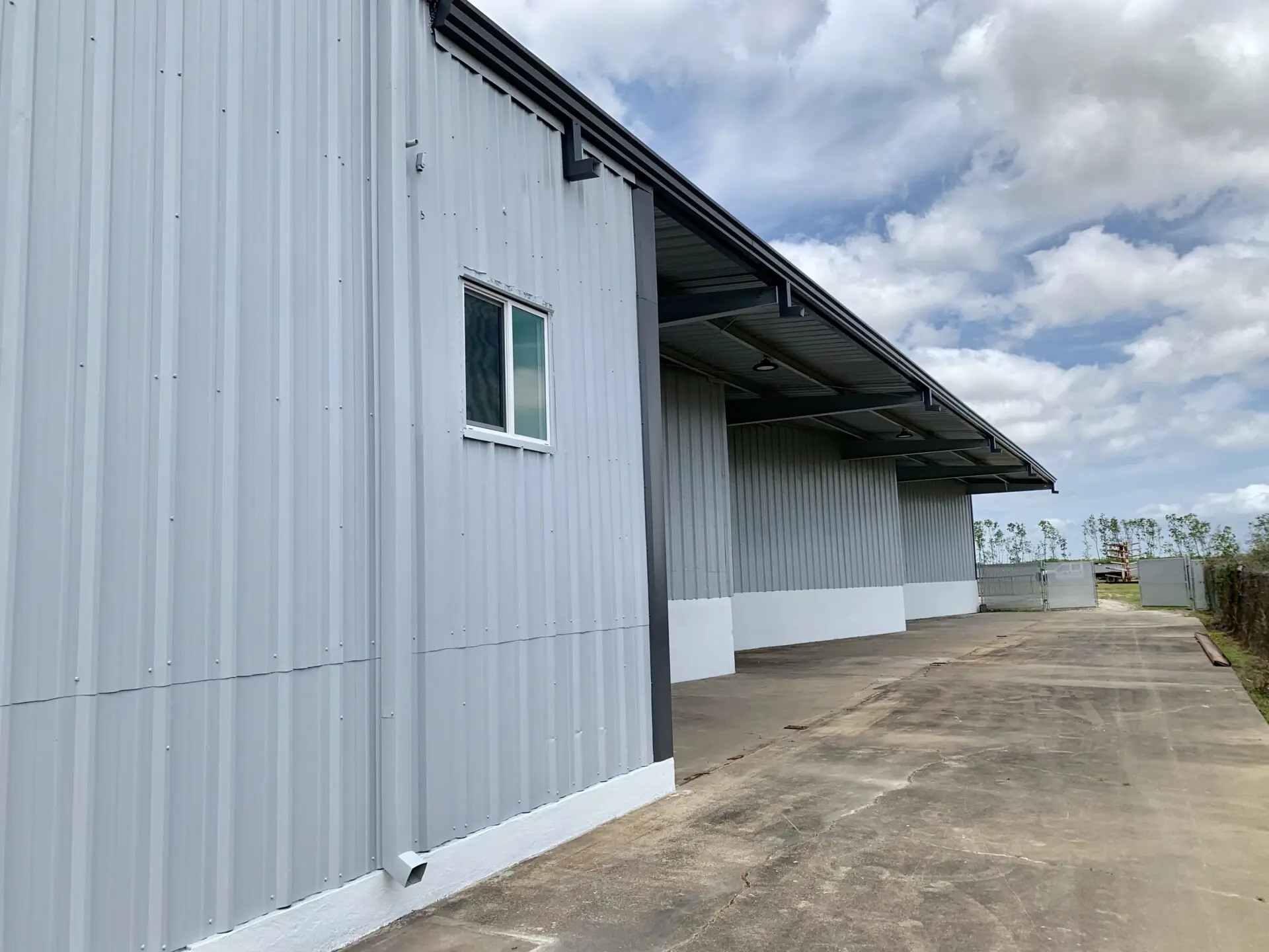 Side elevation of Summit Industrial's renovated warehouse showing gray metal siding, covered laydown area, and open yard for materials and equipment