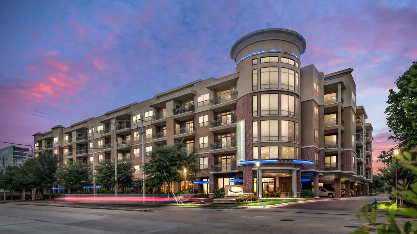 Upper Kirby Apartments exterior at dusk in Houston, TX with a brick and stucco mid-rise building and a signature curved glass tower entry