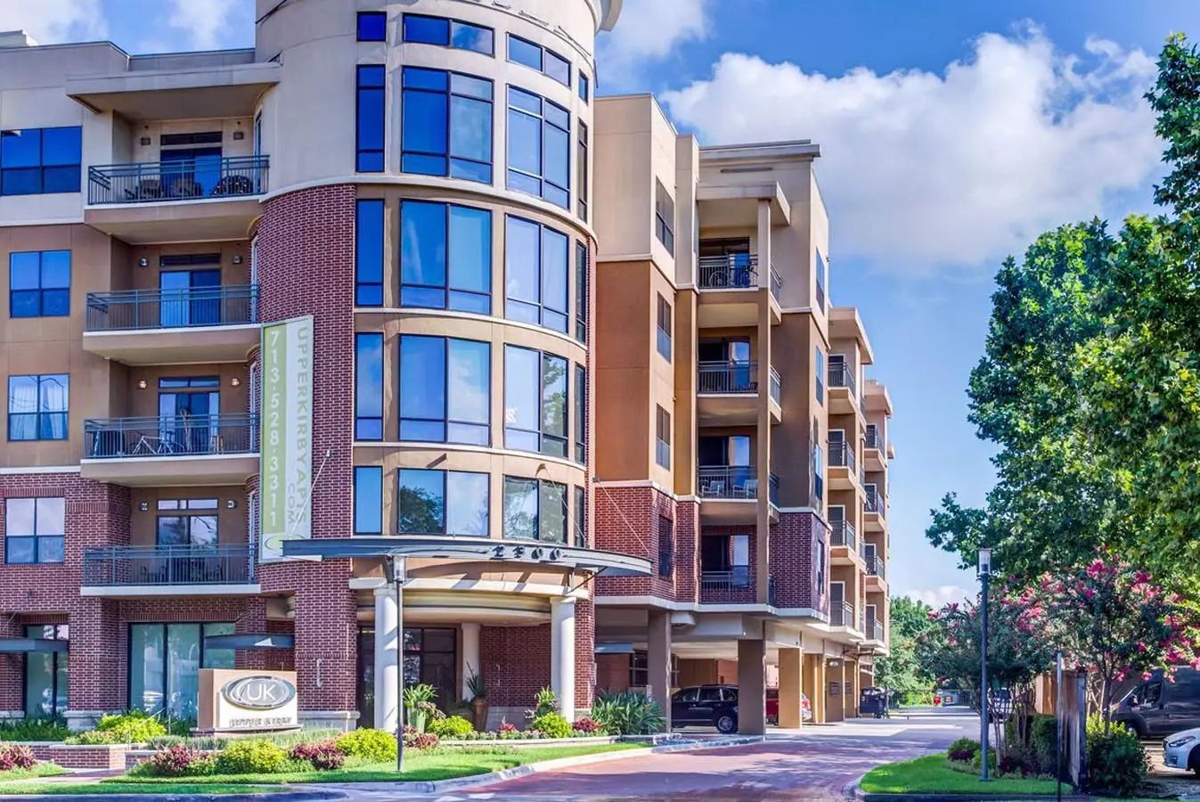 Daytime view of Upper Kirby Apartments in Houston, TX showing the brick facade, curved glass tower, and covered resident drop-off