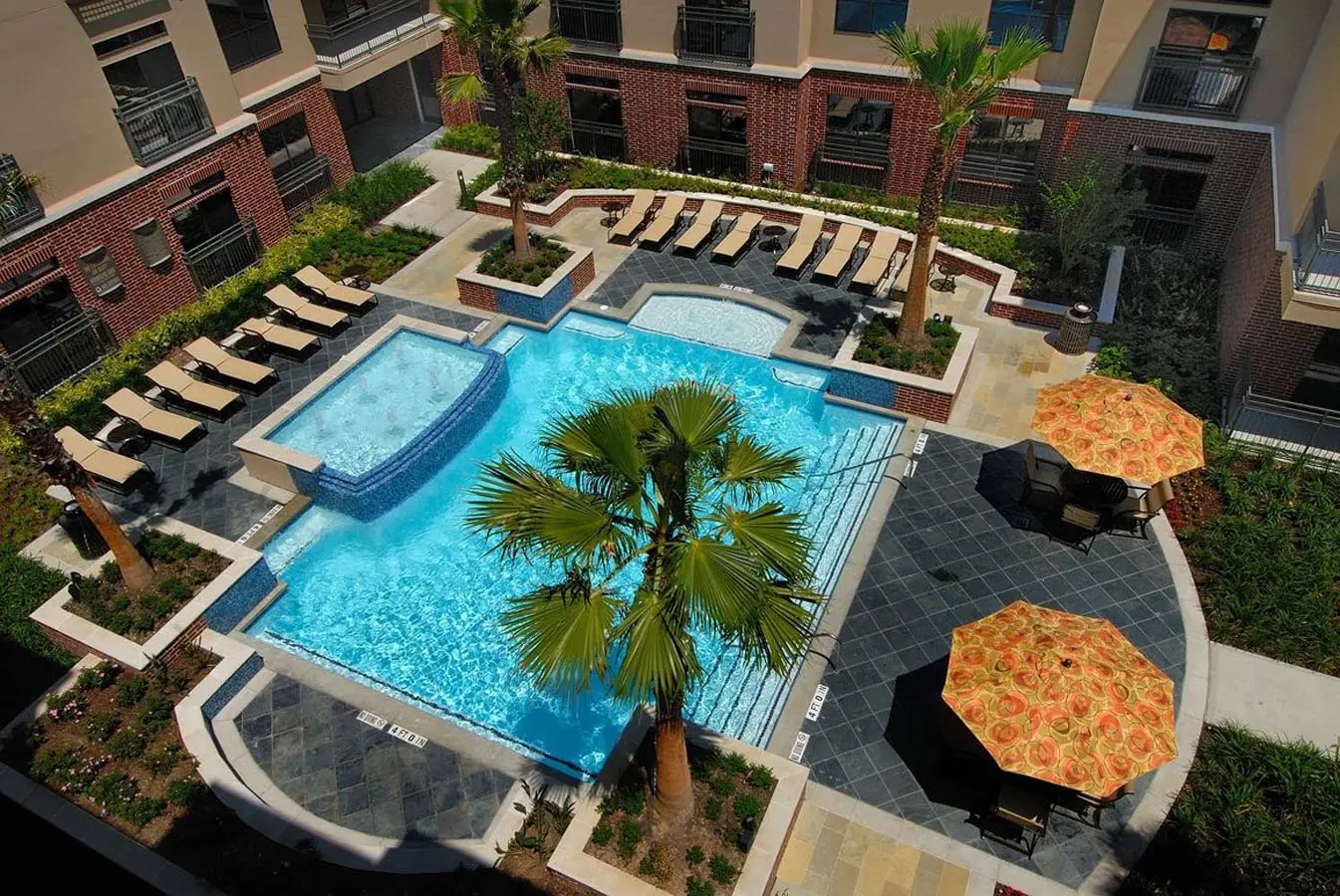 Aerial view of the courtyard pool at Upper Kirby Apartments with palm trees, lounge chairs, hot tub, and shaded patio seating