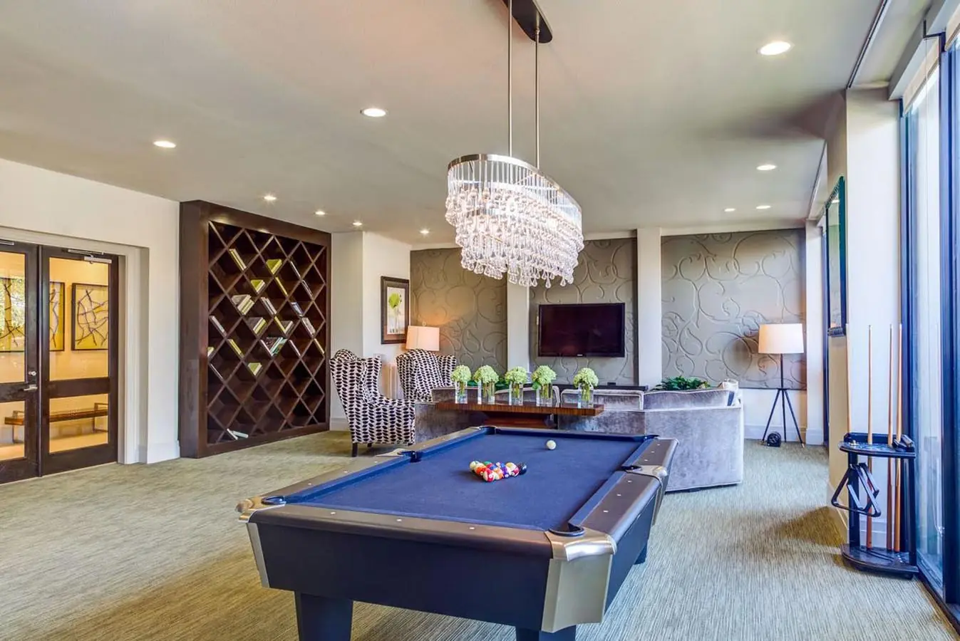 Club-style resident lounge at Upper Kirby Apartments with a blue-felt billiards table, crystal chandelier, lounge seating, and a TV wall