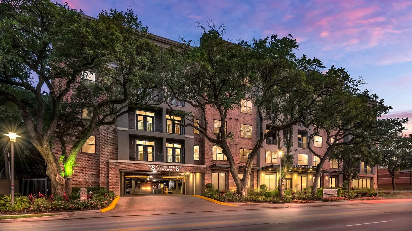 Westheimer Apartments welcome center and parking entry framed by mature oak trees at sunset in Houston, TX